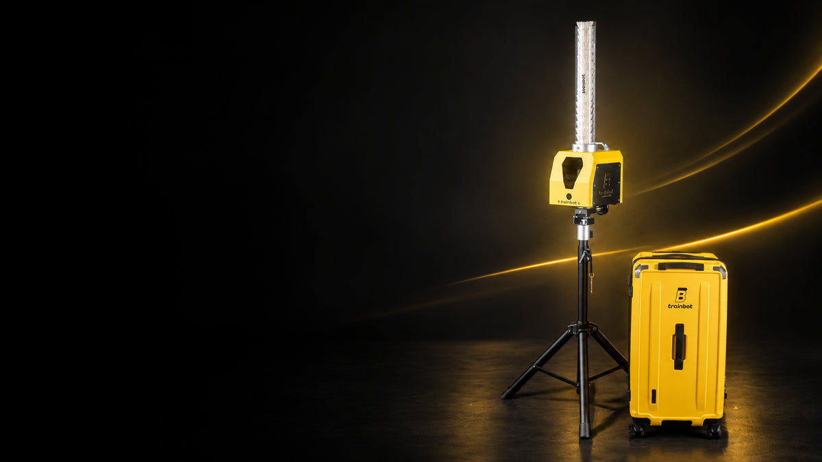 BaddyBot Pro badminton shuttle feeder on its tripod beside the yellow TrainBot transport case, with yellow studio lighting.